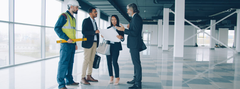 Multi-ethnic group of businesspeople male and female are talking and studying blueprint indoors in modern commercial building. Business and communication concept.